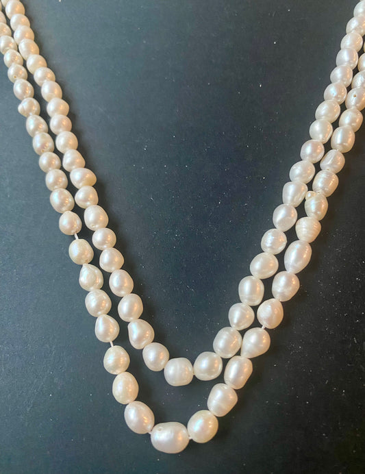 Delicate strands of 6.5mm freshwater smooth baroque pearl beads elegantly displayed on a smooth black surface.
