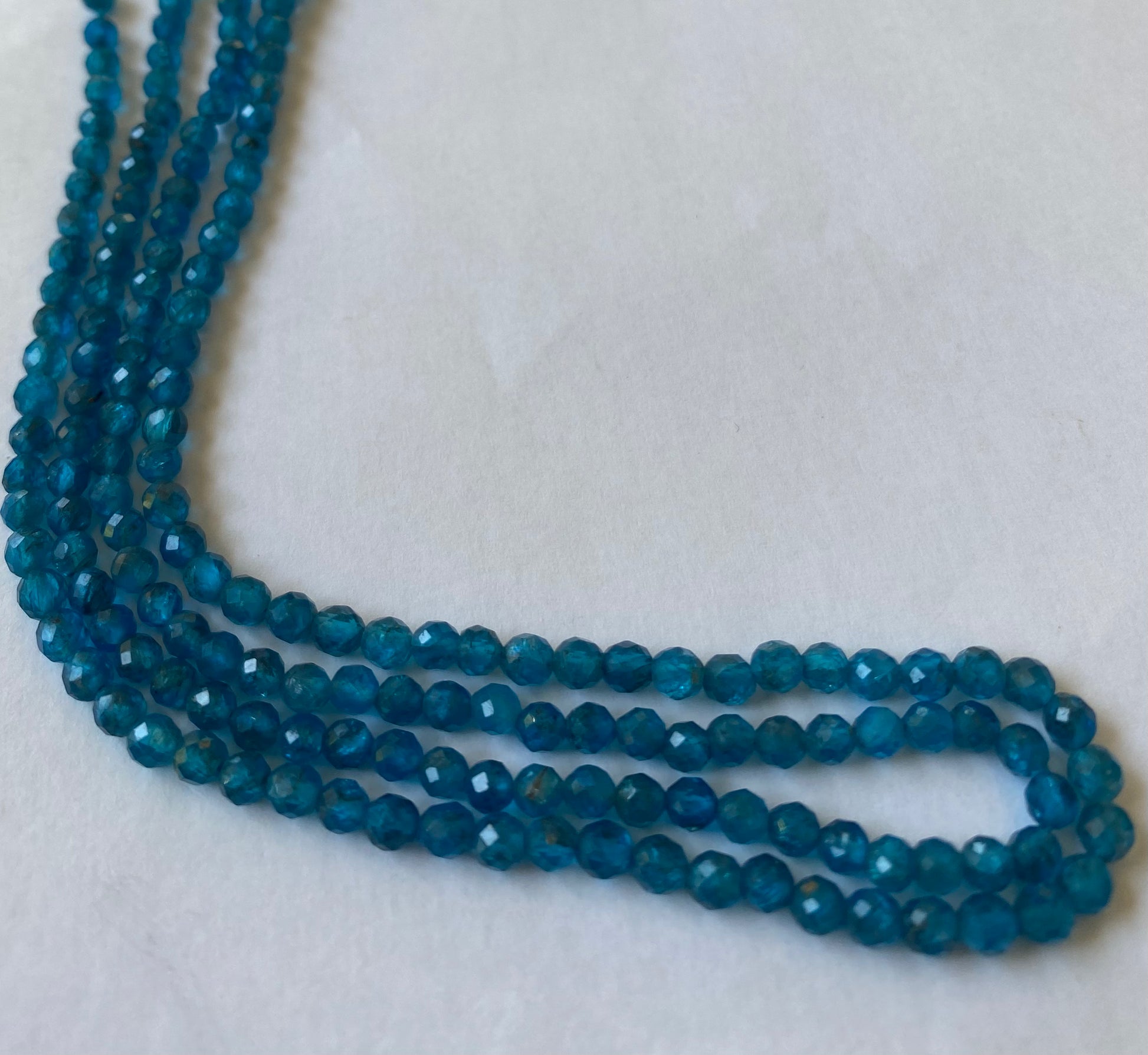  Close-up of a blue gemstone bead strand  highlighting neon apatite faceted rondelle gemstones.