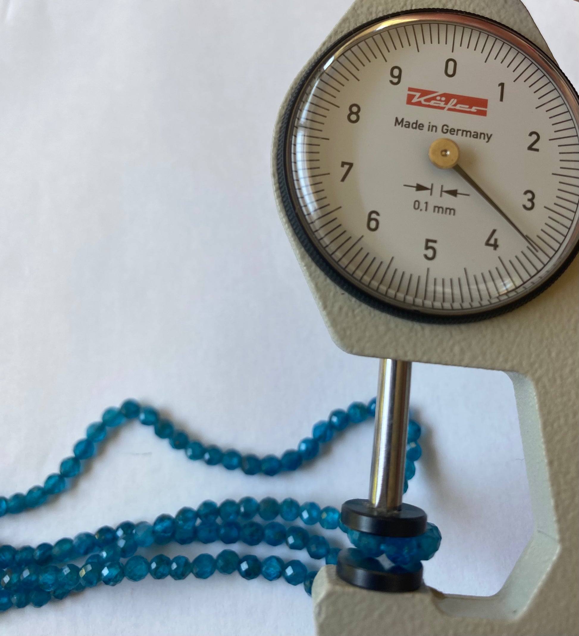 A dial gauge measures the Neon Apatite faceted rondelle gemstone.