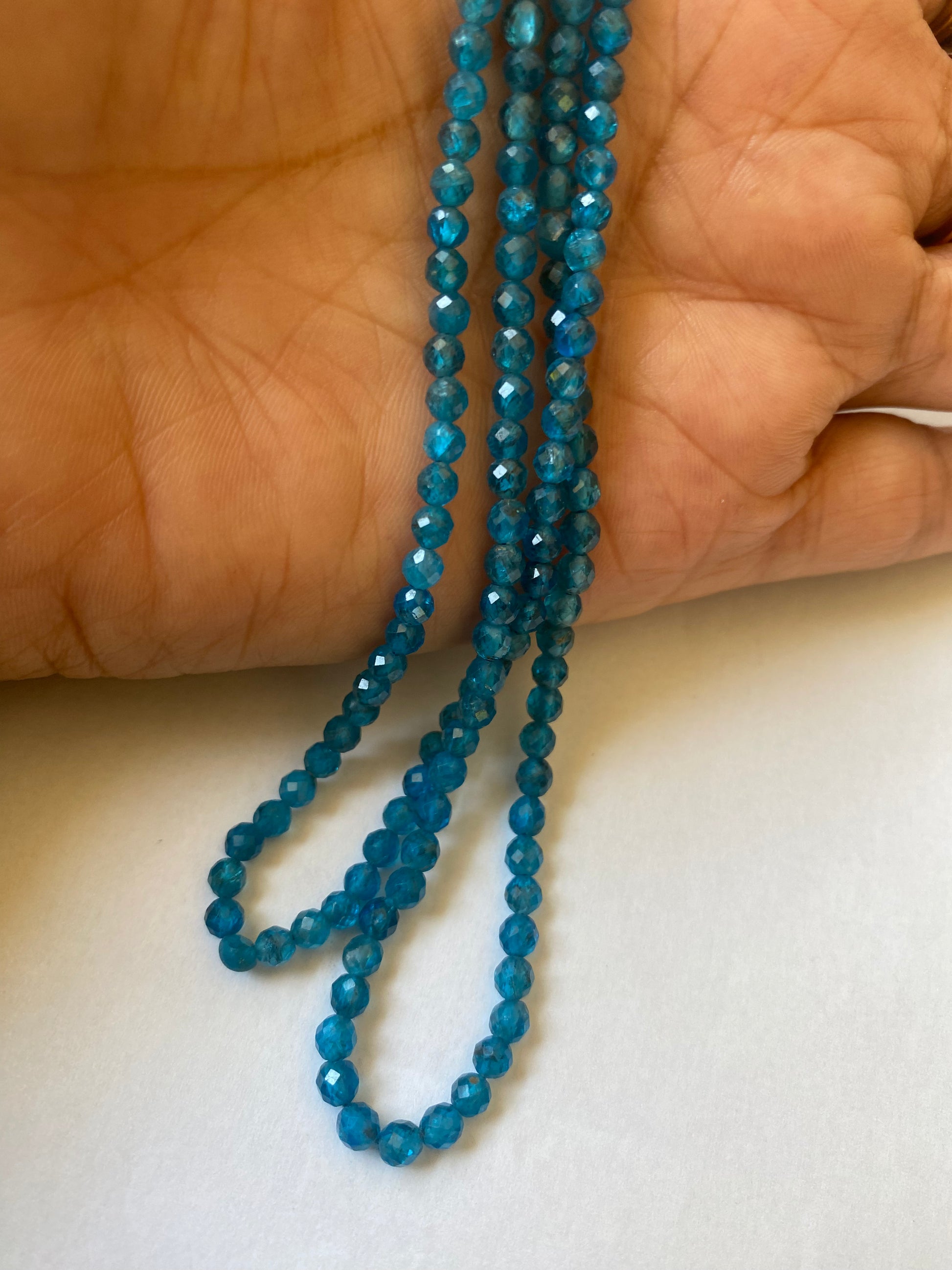 A hand holds a stunning blue strand made of faceted neon apatite rondelle gemstones.