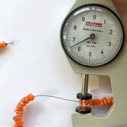 A dial gauge measures the opal chip 3.5-6.5mm gemstone for accurate sizing.