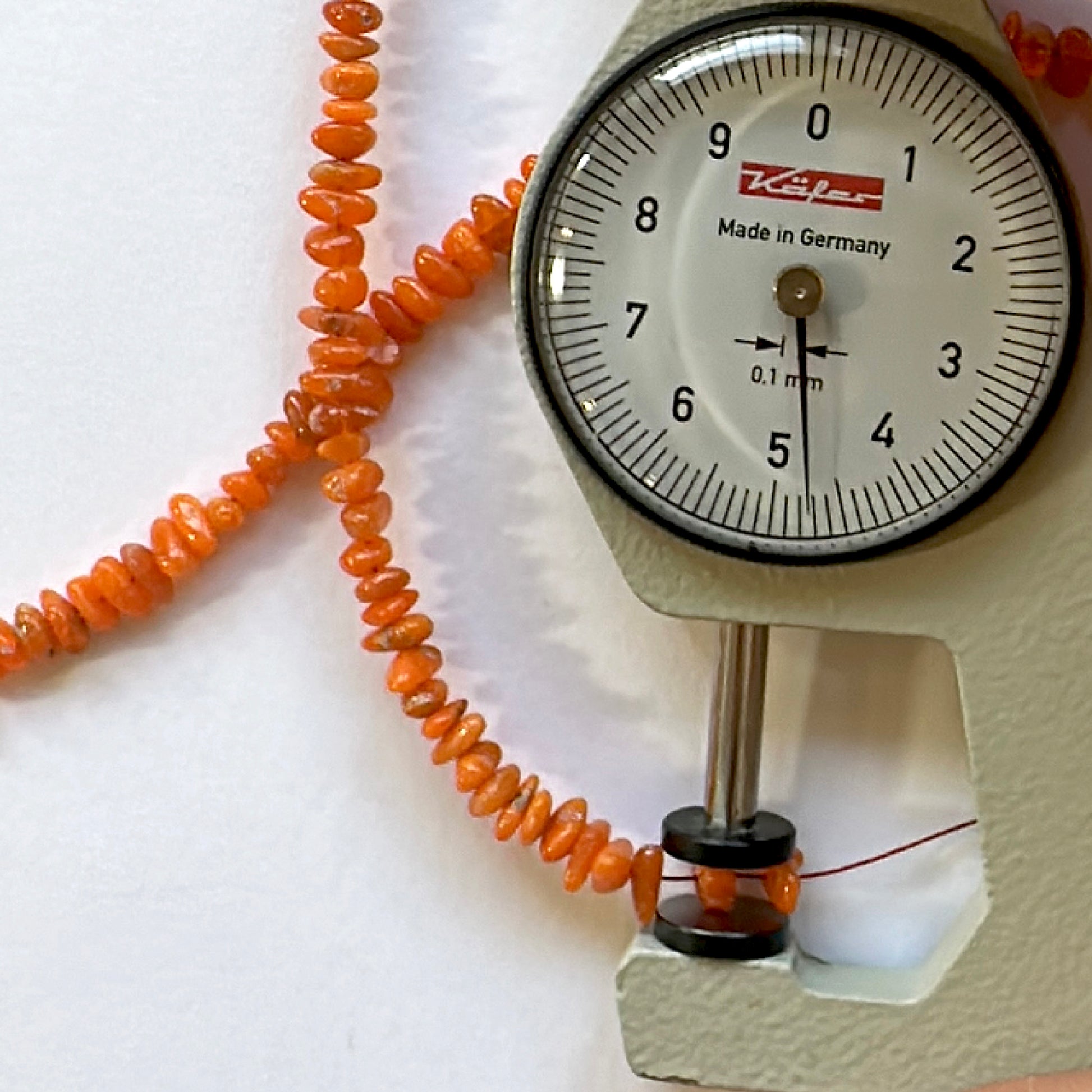 A dial gauge measures the opal chip 3.5-6.5mm gemstone for accurate sizing.