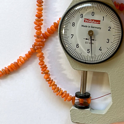 A dial gauge measures the opal chip 3.5-6.5mm gemstone for accurate sizing.
