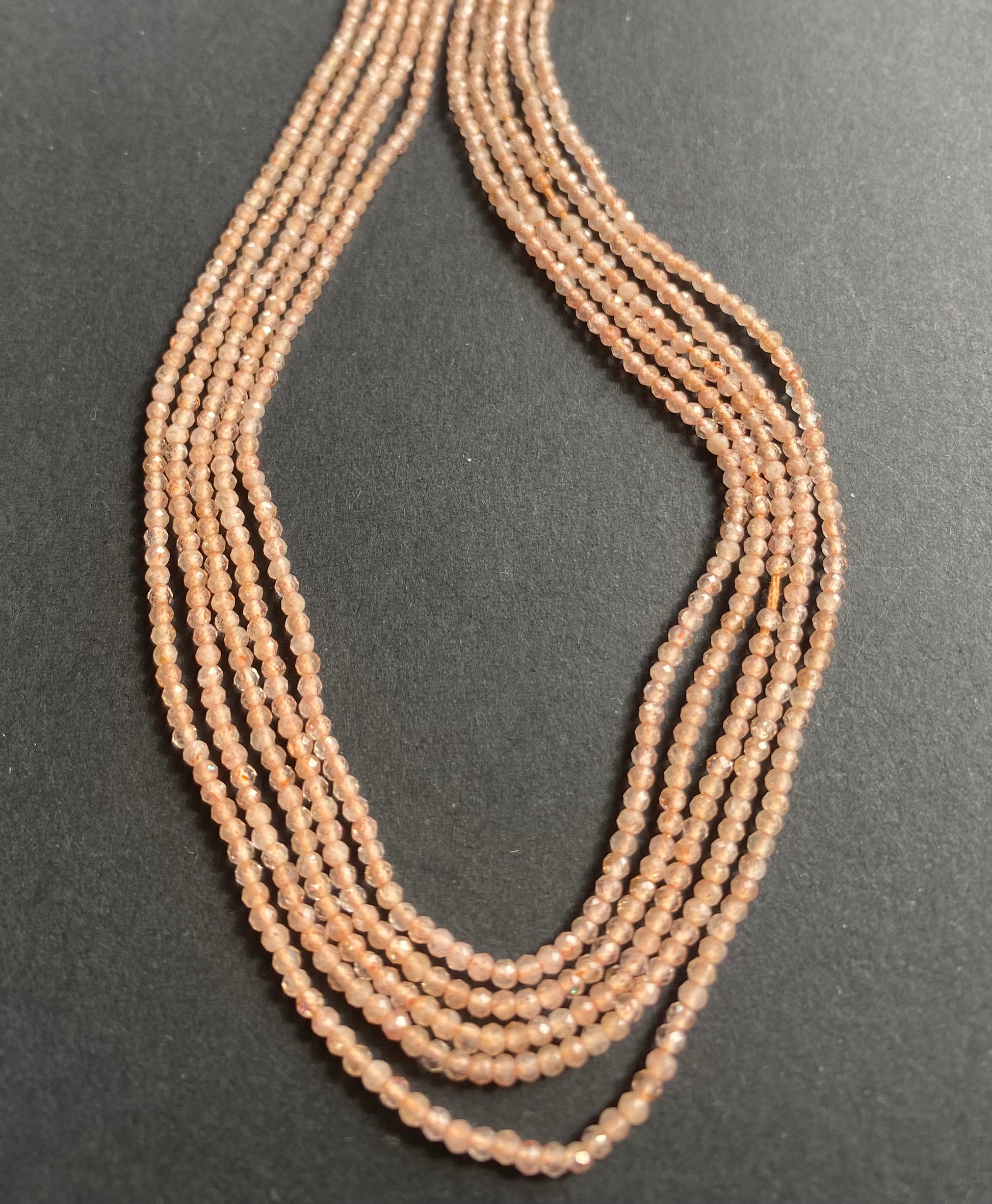 Delicate peach moonstone rondelle beads glimmer on a sleek black background, highlighting their soft, warm hue.