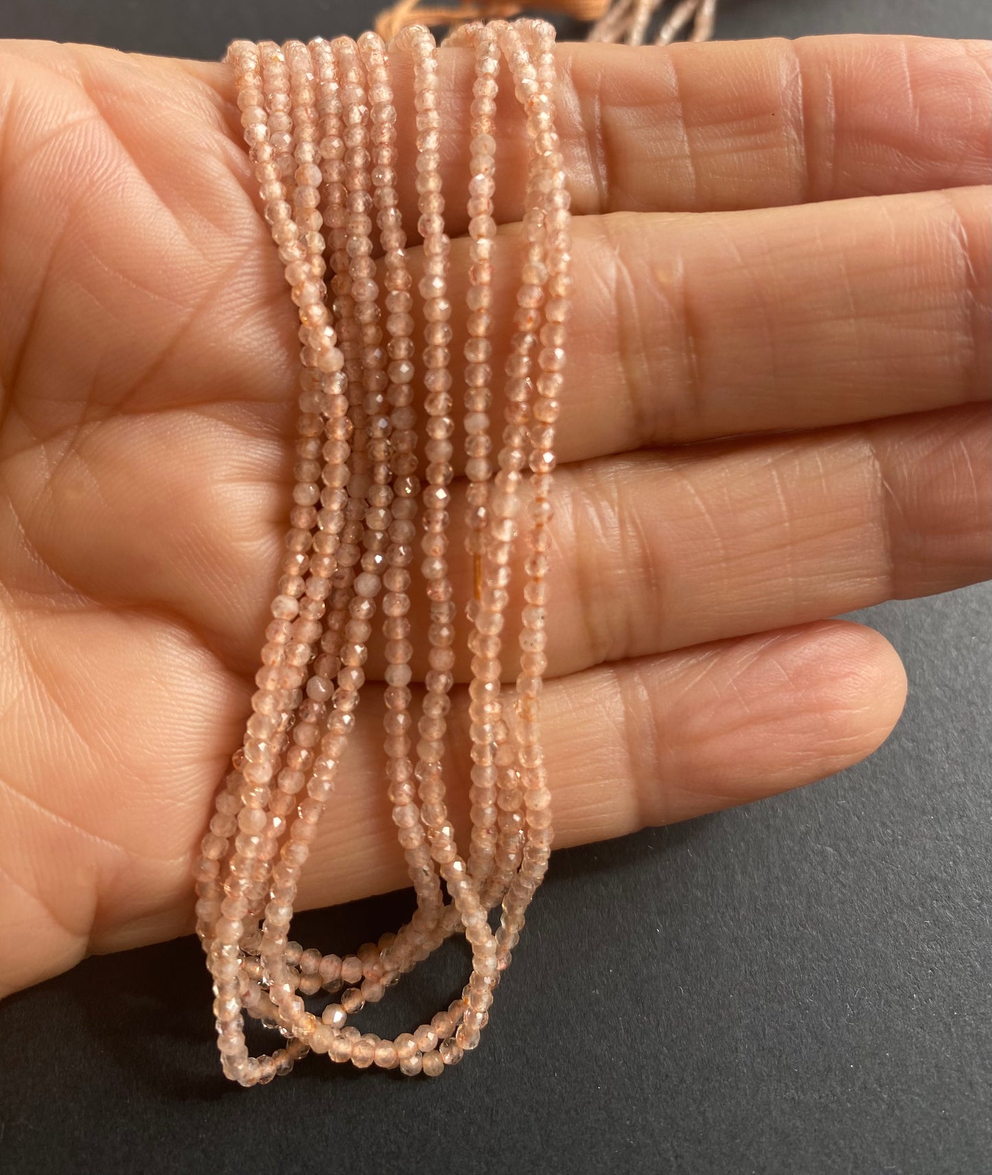 A person holds delicate strands of pink peach moonstone beads, showcasing their micro-faceted rondelle design.