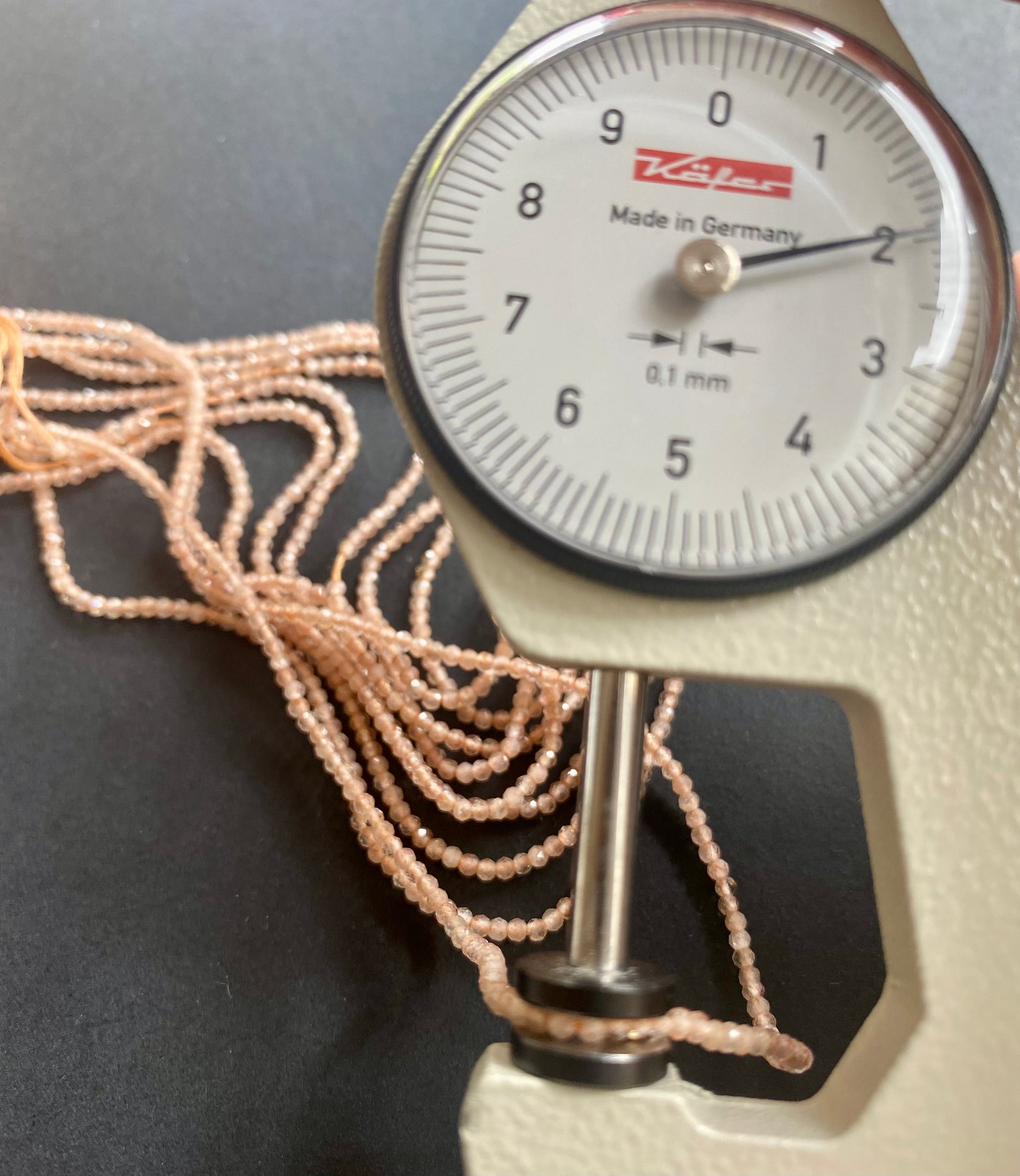 Close-up view of a dial gauge  with peach moonstone beads, measuring 2mm, highlighting their glossy finish.