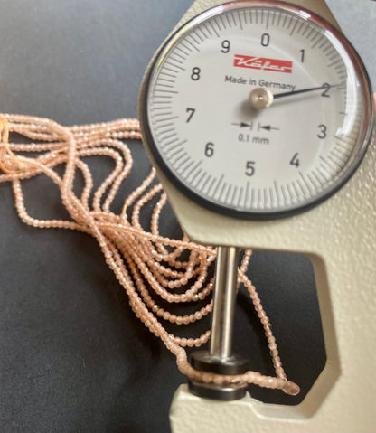 Close-up view of a dial gauge  with peach moonstone beads, measuring 2mm, highlighting their glossy finish.