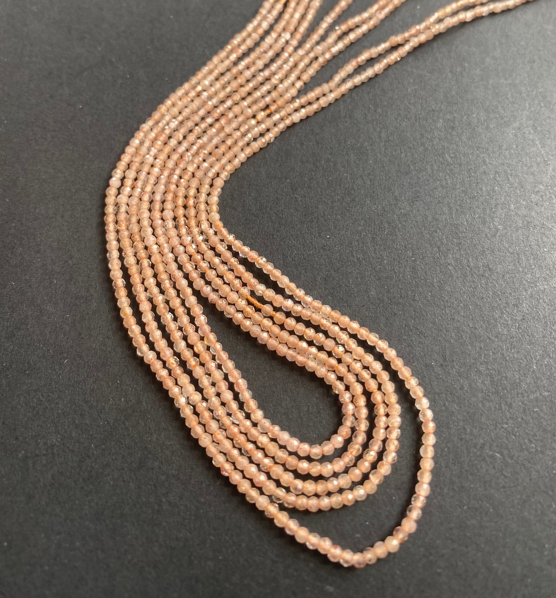 Beautiful strands of 2mm peach moonstone beads lies on a dark surface, emphasising their subtle lustre and elegance.