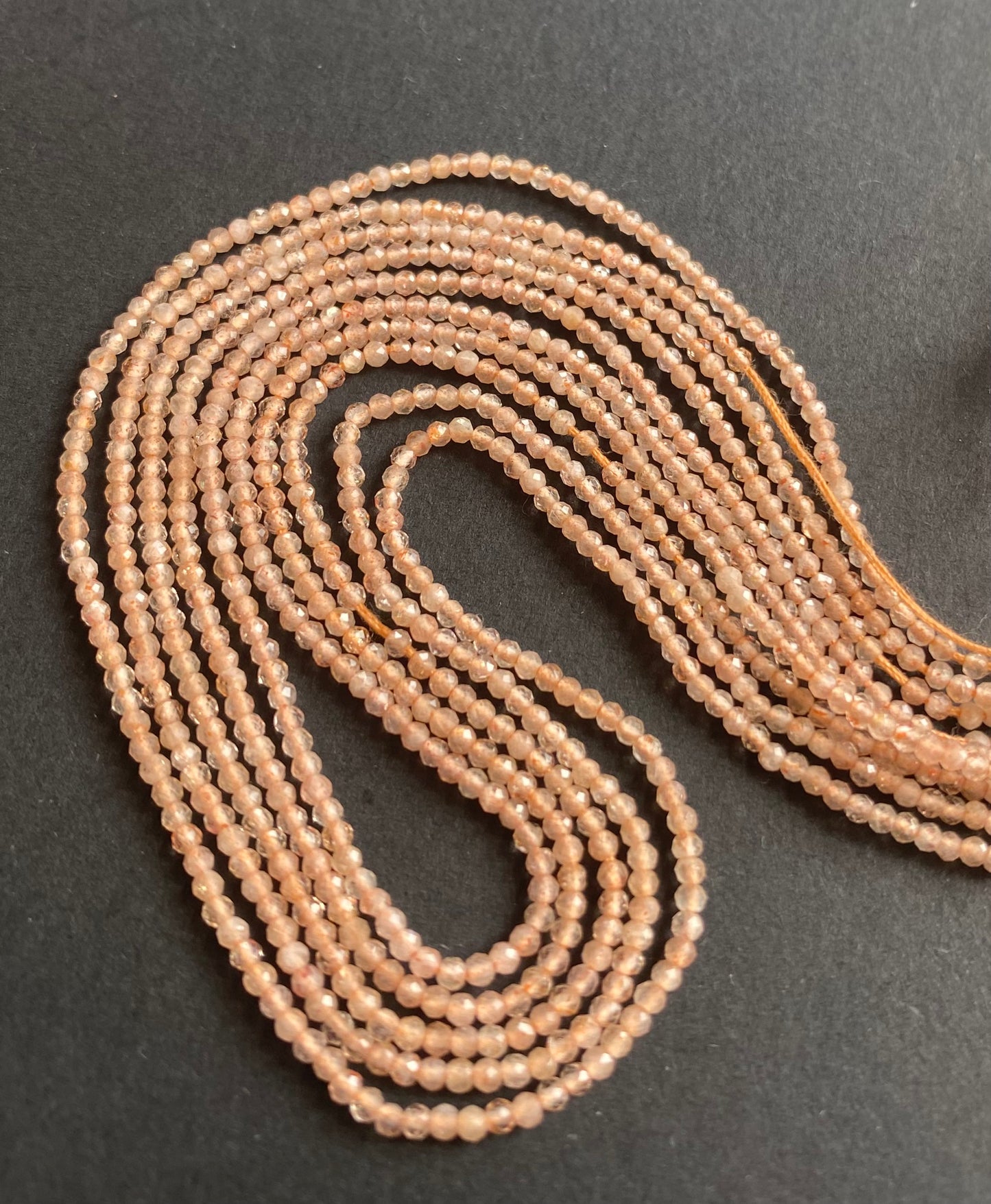 Elegant peach moonstone beads are arranged on a black surface, their soft colour and shine creating a captivating display. Ideal for delicate jewellery making.