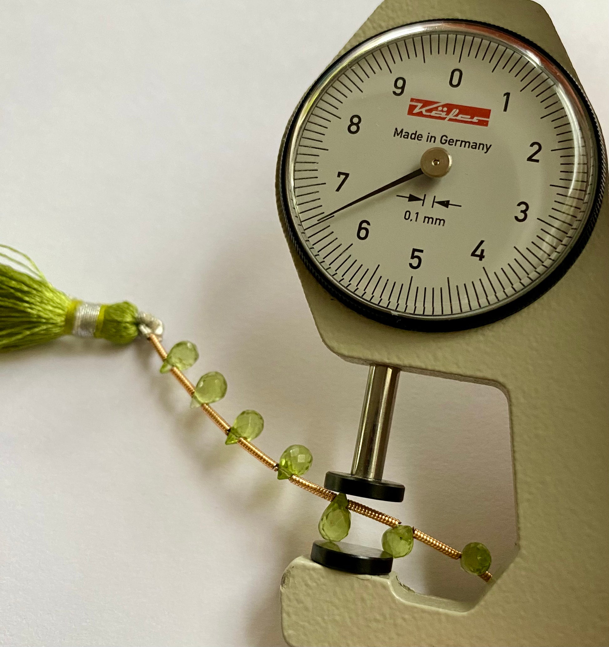 A close-up of a person measuring a peridot faceted briolette  3.7mm-to-4.4mm bead stone, with  dial gauge.