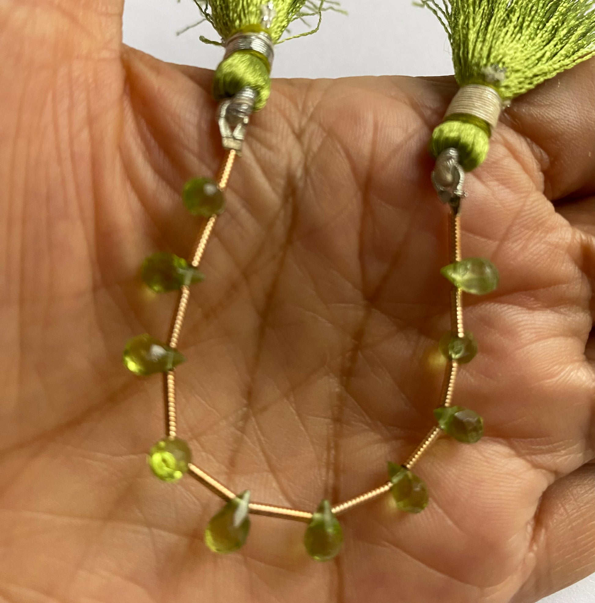 A hand displays a beautiful green briolette peridot gemstone beads, emphasising its faceted design and vibrant colour.