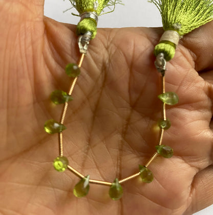 A hand displays a beautiful green briolette peridot gemstone beads, emphasising its faceted design and vibrant colour.