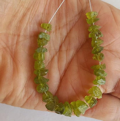 A hand holding a cluster of green peridot gemstone beads, showcasing their rough texture and vibrant colour.