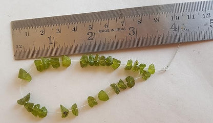 A ruler placed next to a group of green peridot beads, each measuring between 7mm and 8.5mm.