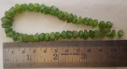 A ruler beside a peridot natural gemstone bead, measuring 7mm-to-9mm in diameter.