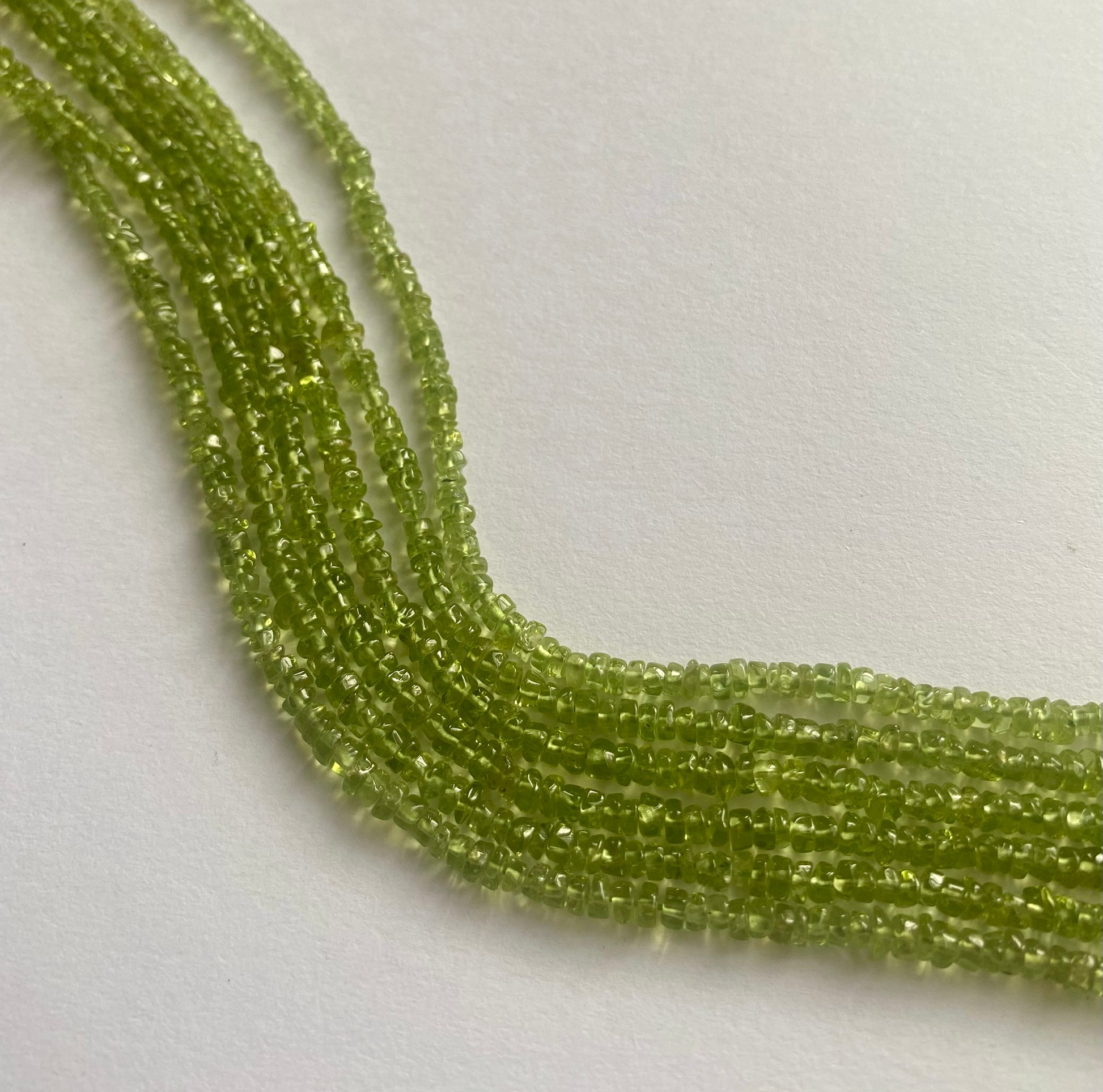 A close-up of a strands of smooth green peridot beads, measuring 3.5mm to 4mm, highlighting their rich, vibrant hue.  
