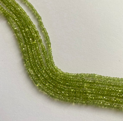 A close-up of a strands of smooth green peridot beads, measuring 3.5mm to 4mm, highlighting their rich, vibrant hue.  