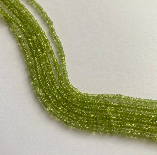 A close-up of a strands of smooth green peridot beads, measuring 3.5mm to 4mm, highlighting their rich, vibrant hue.  