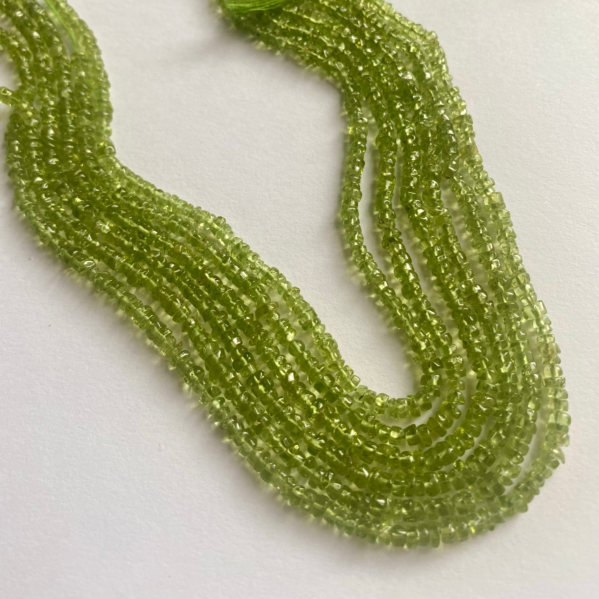 Strands of polished green peridot beads, 3.5mm to 4mm, displaying a bright and eye-catching green colour.  