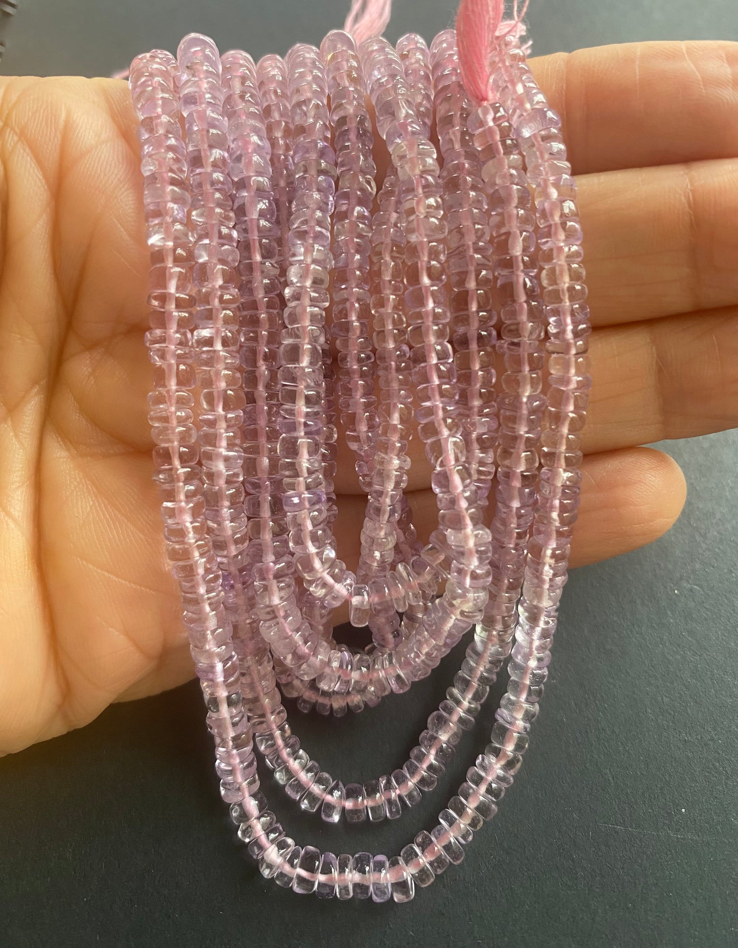  A person holding a smooth wheel amethyst gemstone strand, showcasing its pink facets and elegant design.