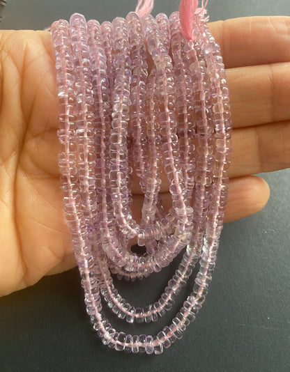  A person holding a smooth wheel amethyst gemstone strand, showcasing its pink facets and elegant design.