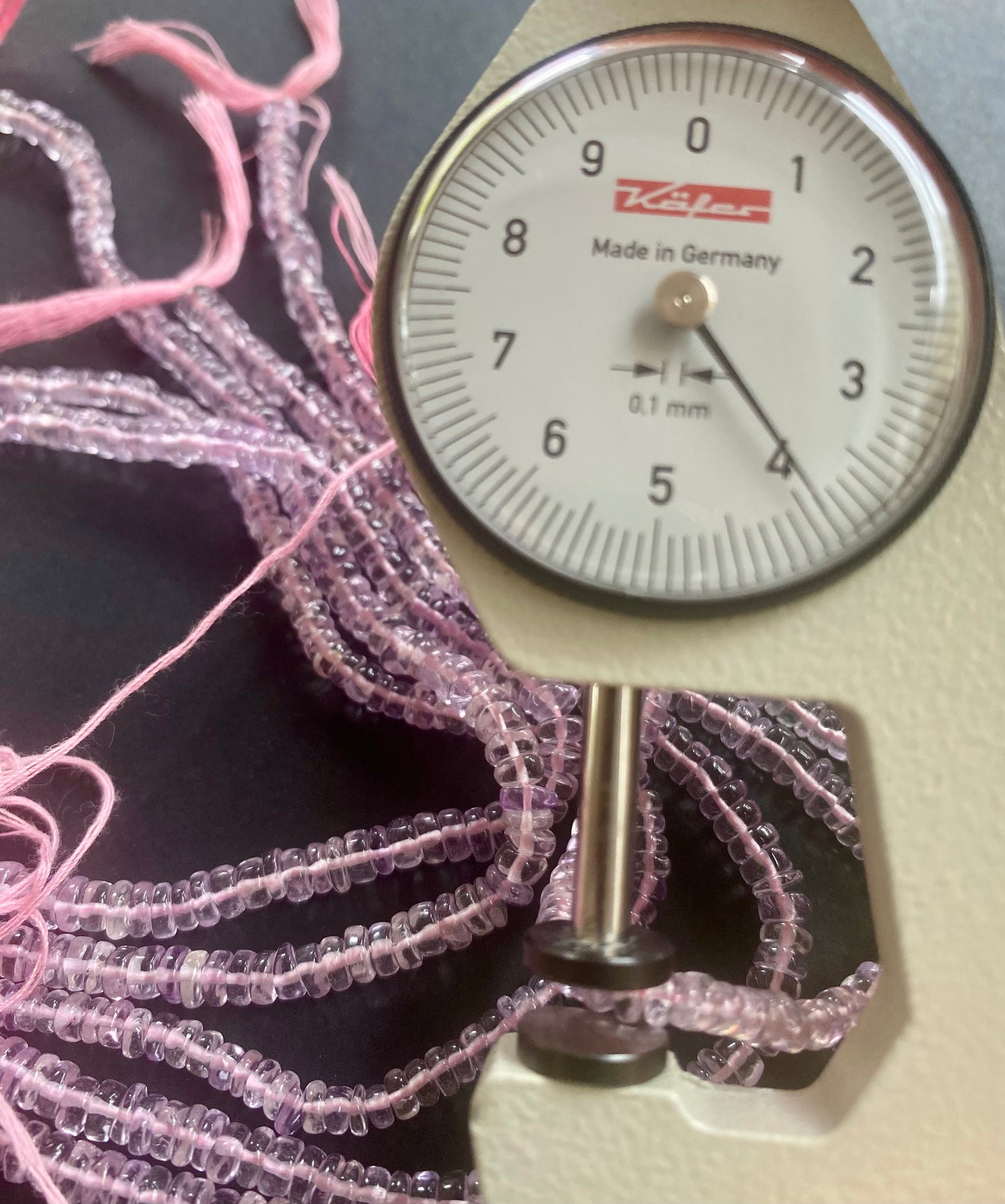 A person measures a purple amethyst teardrop stone, ranging from 3.5mm to 4.5mm mm , using a dial gauge measuring tool.
