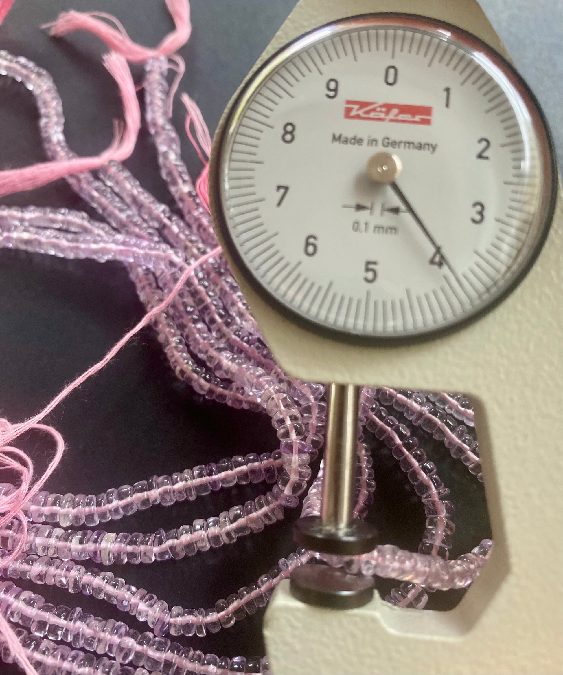 A person measures a purple amethyst teardrop stone, ranging from 3.5mm to 4.5mm mm , using a dial gauge measuring tool.
