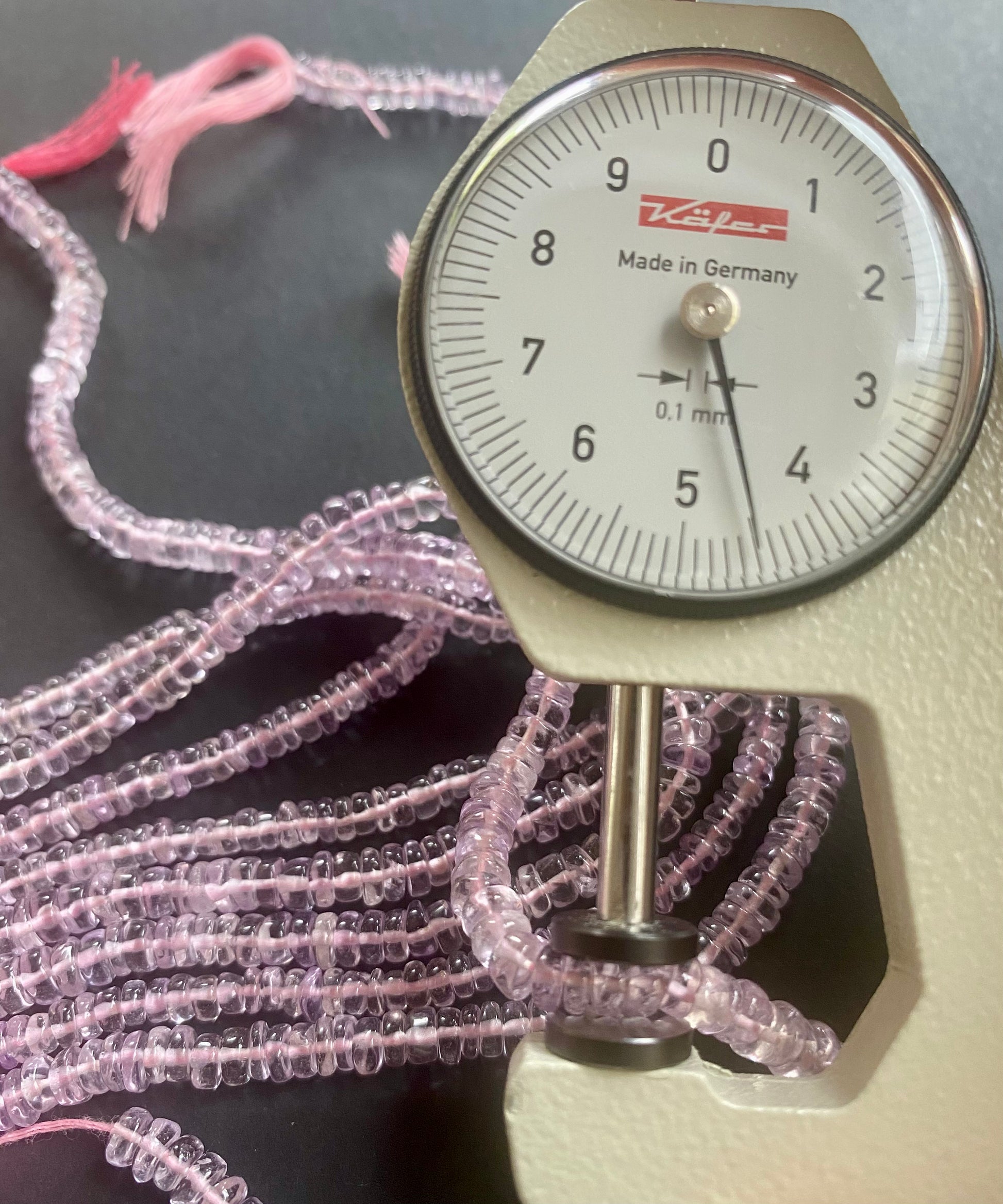A close-up of a person measuring a pink amethyst stone, with  dial gauge.