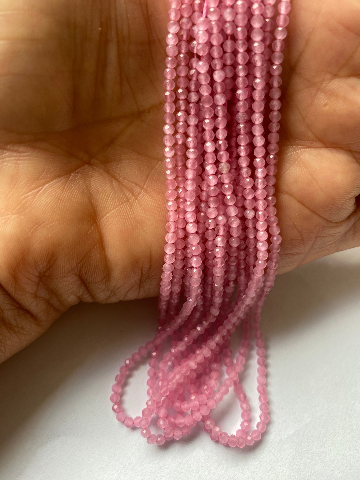 A person holding a strands of pink quartz beads, showcasing their vibrant colour and faceted rondelle shape. 