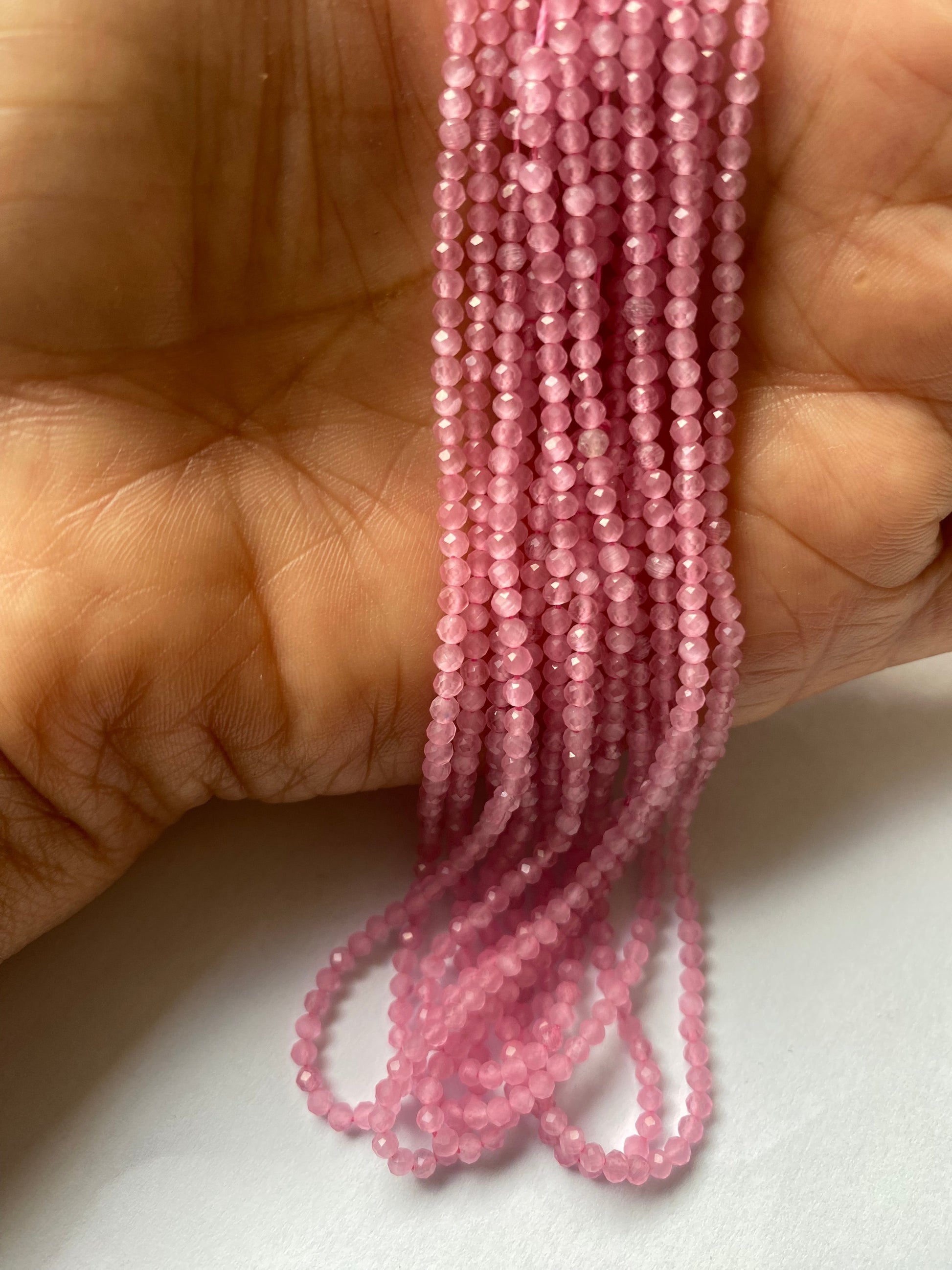 A person holding a strands of pink quartz beads, showcasing their vibrant colour and faceted rondelle shape. 