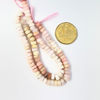 A coin is placed near delicate strands of Pink Shaded Opal beads for scale.