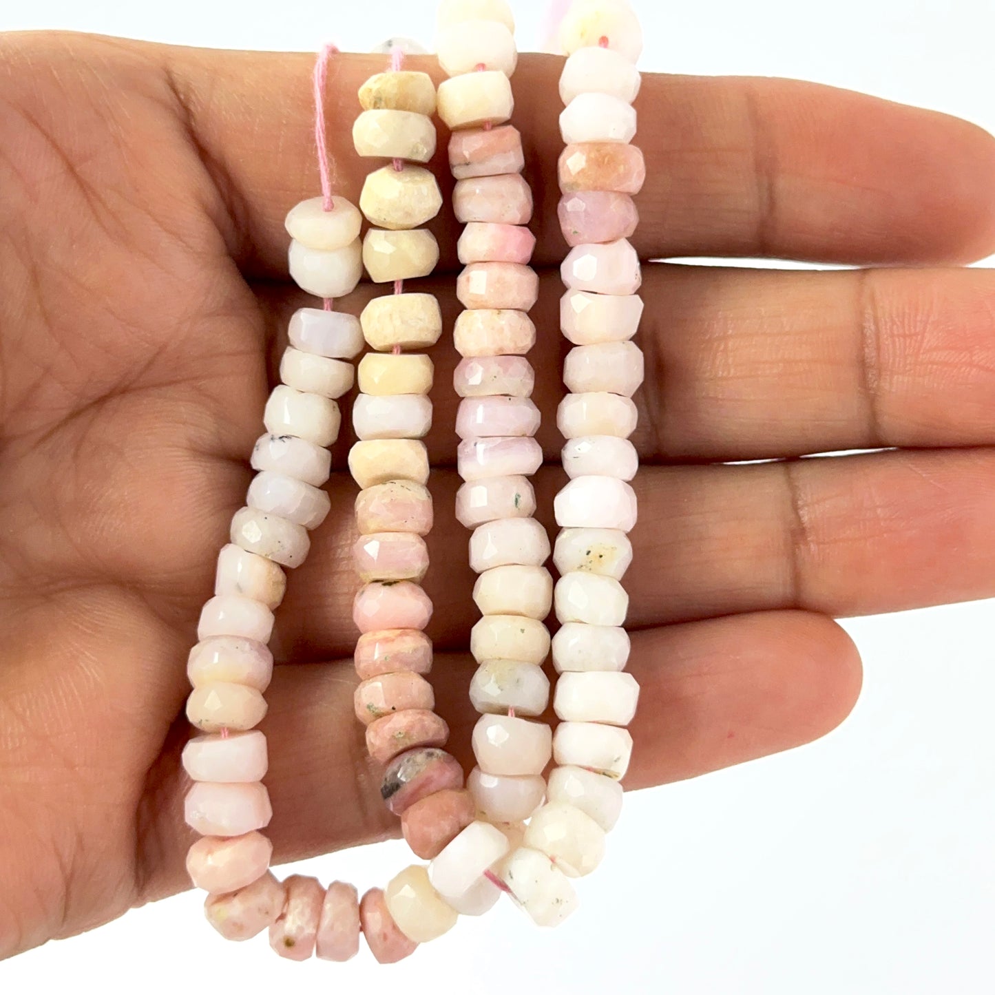 A person holds delicate strands of Pink Shaded Opal beads, showcasing their faceted rondelle design.