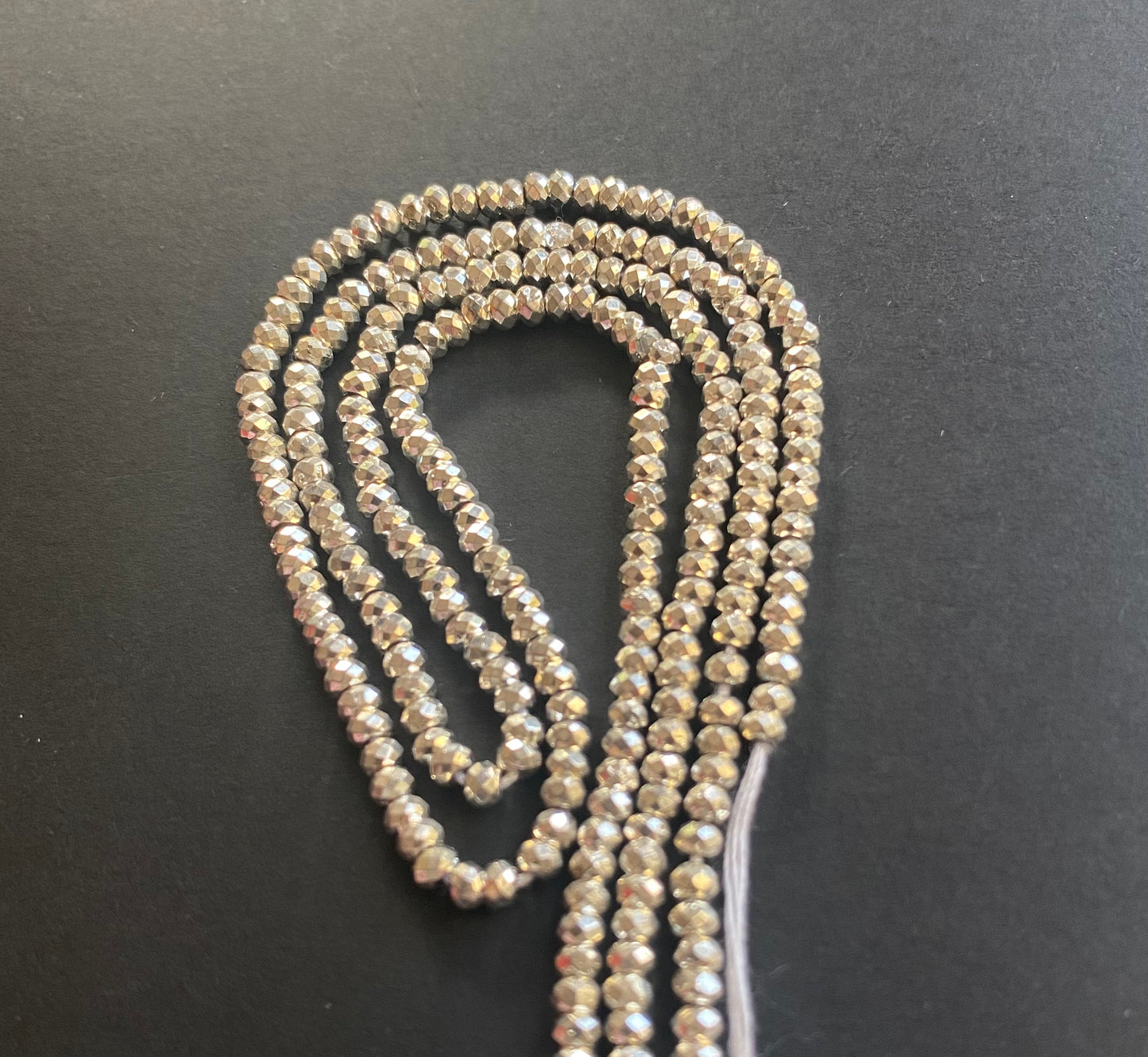 A strand of lustrous 3.1mm pyrite beads laid out on a dark black surface, highlighting their elegance.