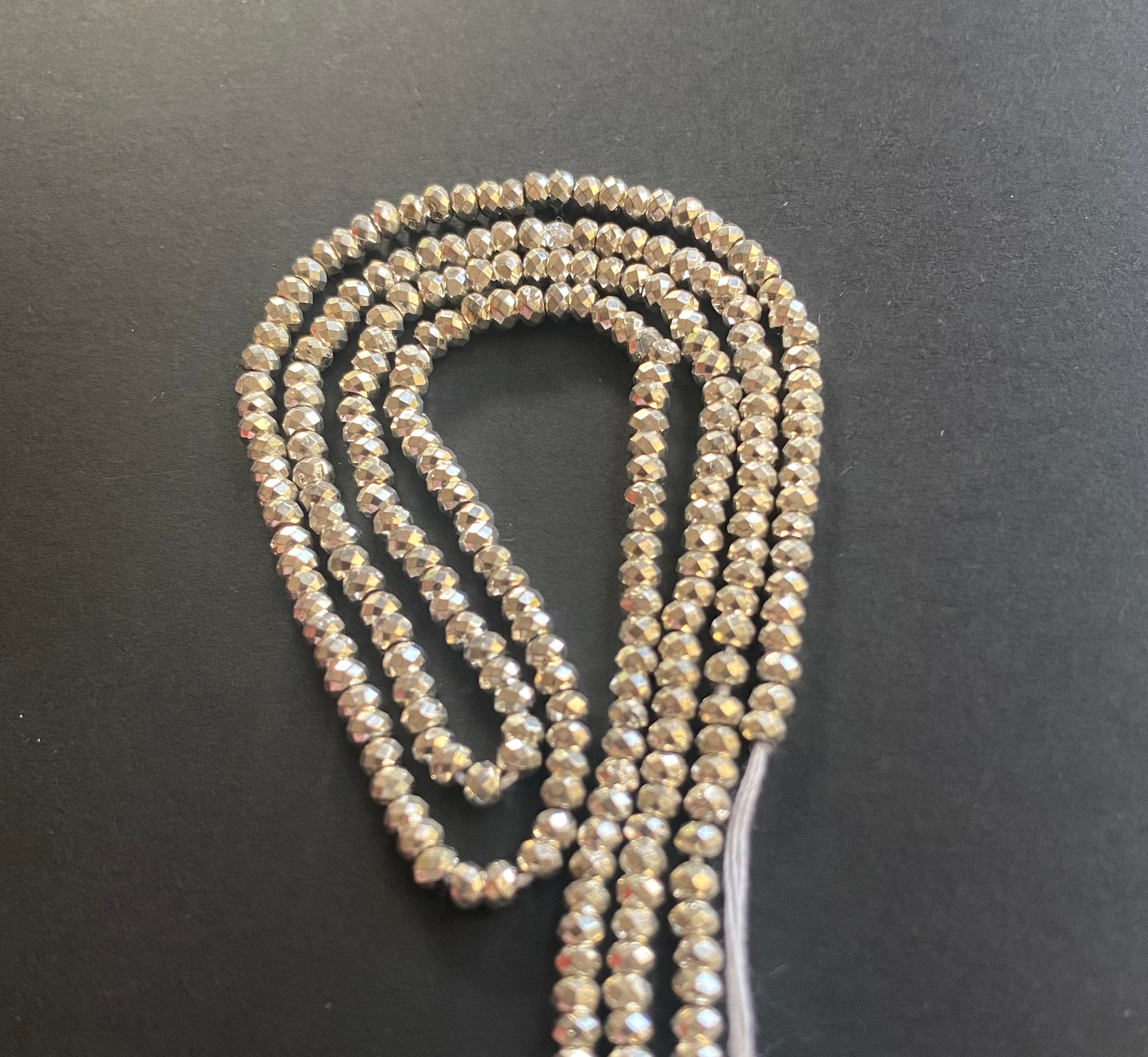 A strand of lustrous 3.1mm pyrite beads laid out on a dark black surface, highlighting their elegance.
