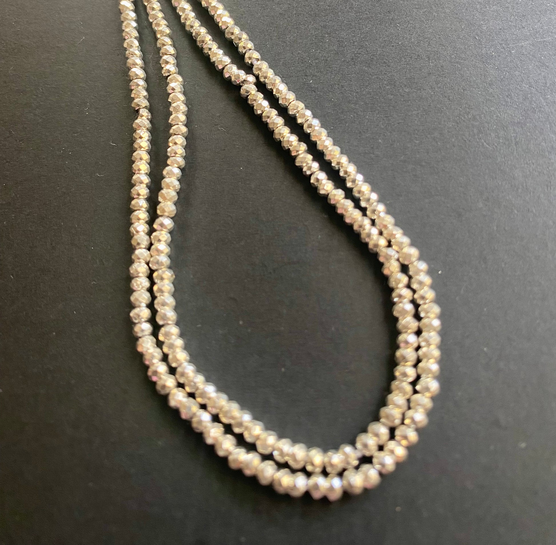 A beautiful strand of 3.1mm pyrite beads resting on a sleek black background, showcasing their lustre.