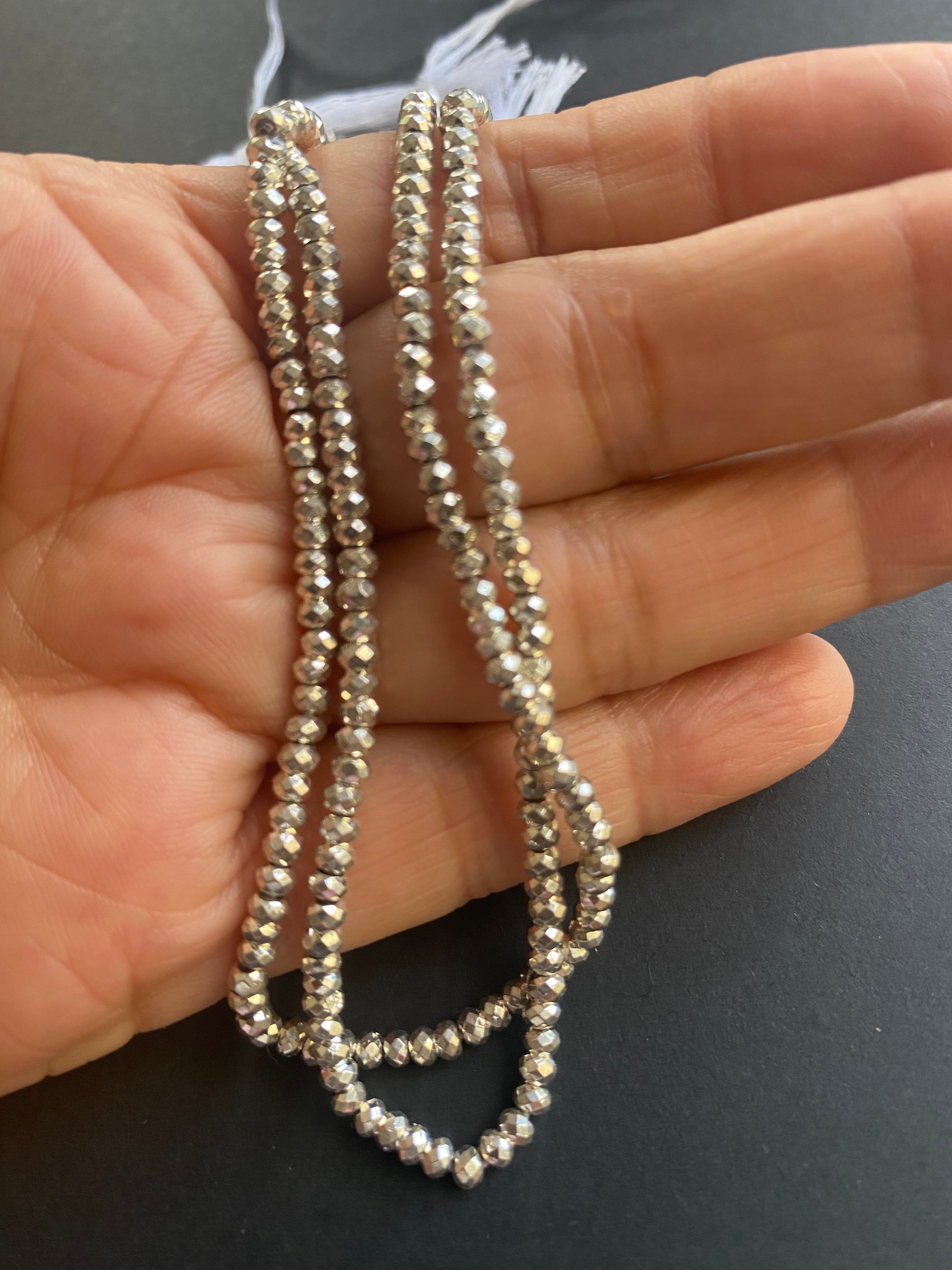 A hand grips a beautiful strand of 3.1mm faceted rondelle pyrite, highlighting their smooth texture and shine.