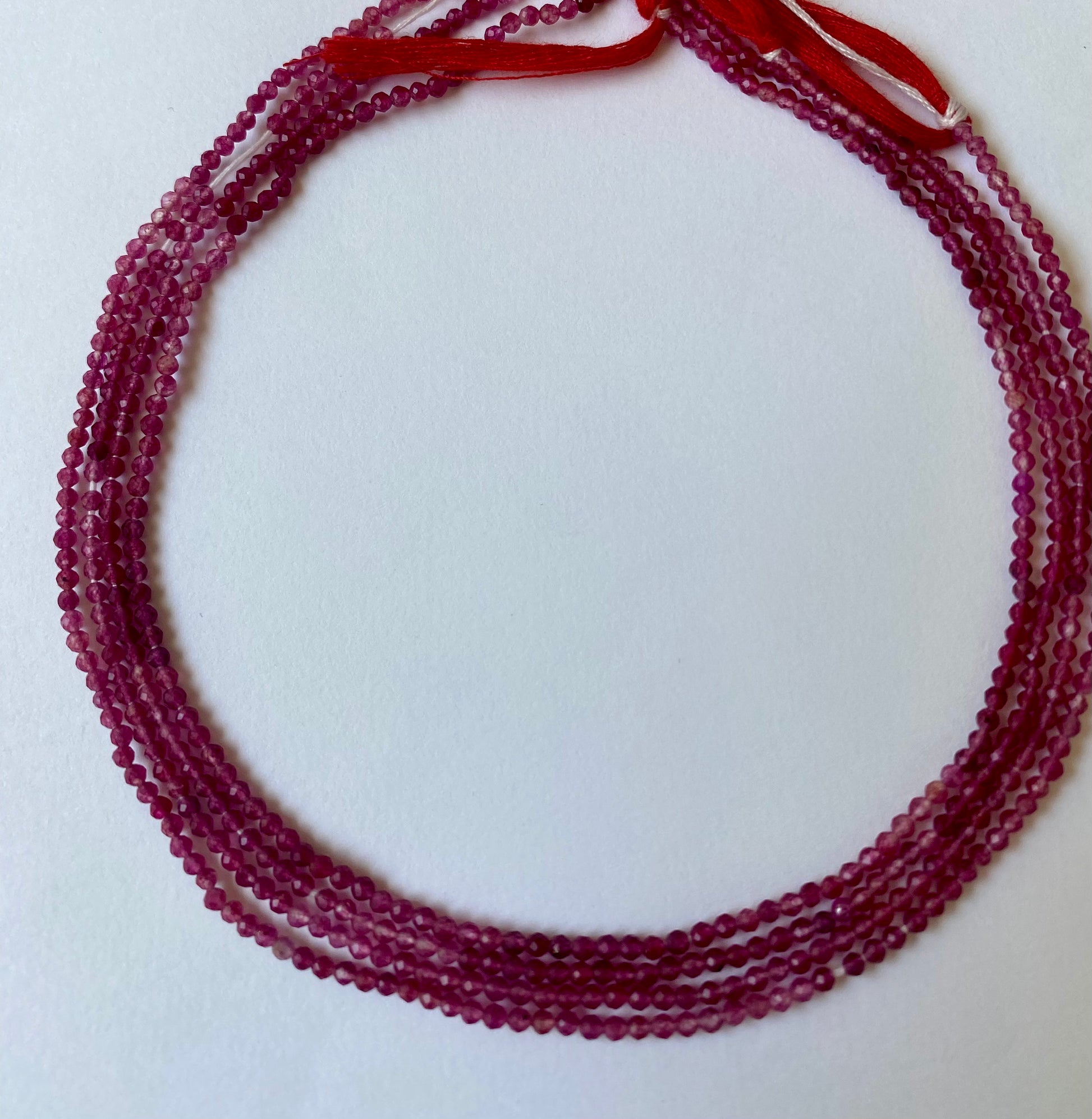 Delicate pink strawberry quartz beads, 2-2.2mm, arranged in a strand on a pristine white background.