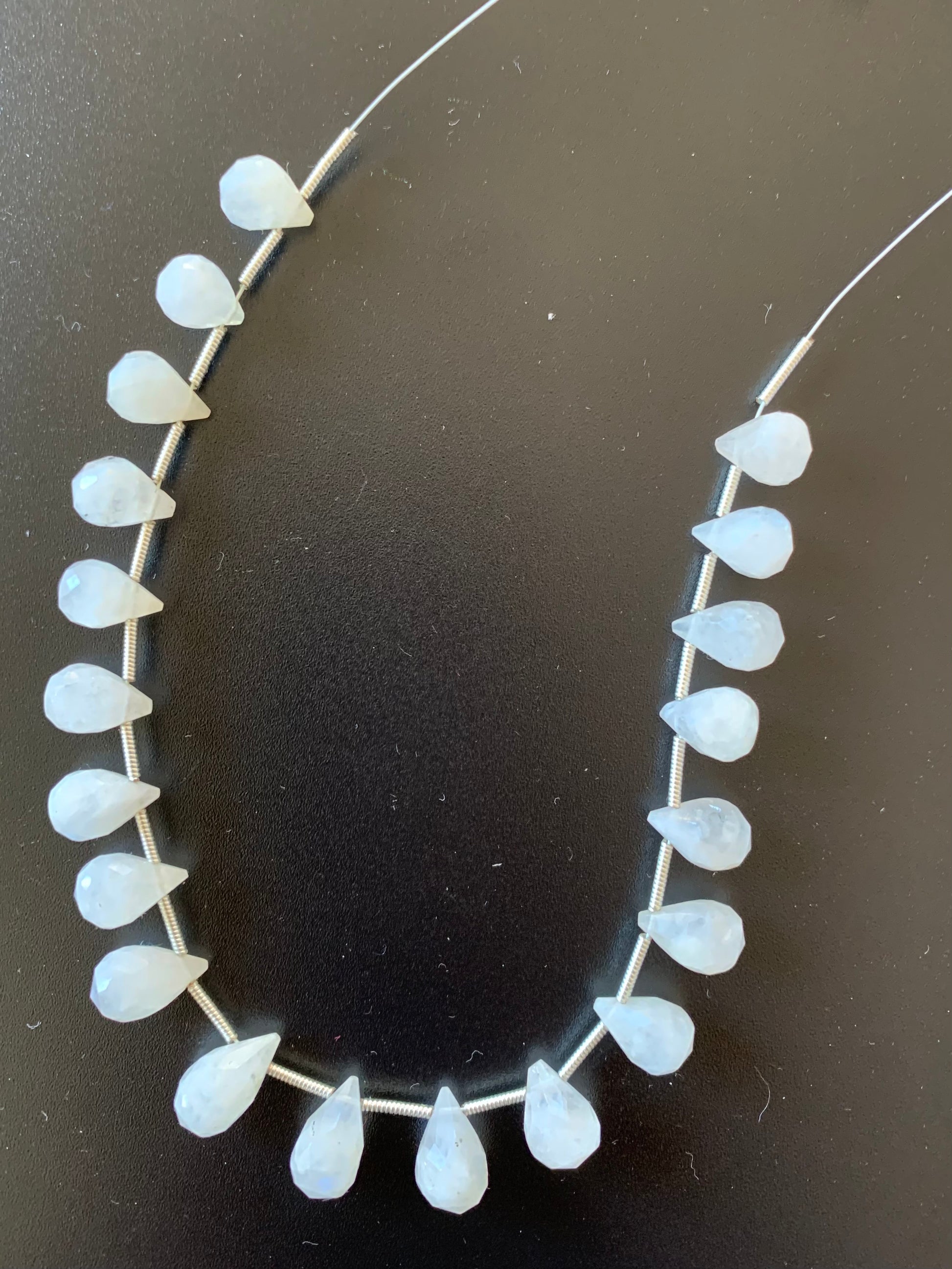 Elegant moonstone beads are arranged on a black surface, their soft colour and shine creating a captivating display.
