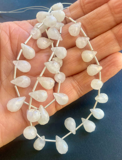 A person holds delicate strands of white moonstone beads, showcasing their tear drop faceted design.