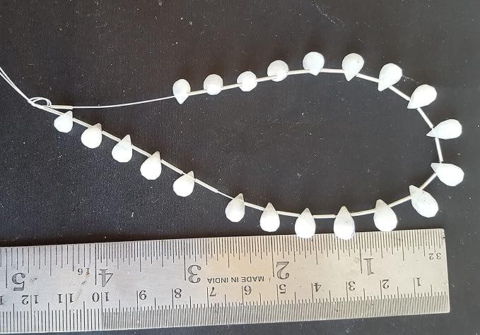 A stylish strand composed of white beads, highlighted by shimmering rainbow moonstone faceted teardrop beads, placed with a ruler.