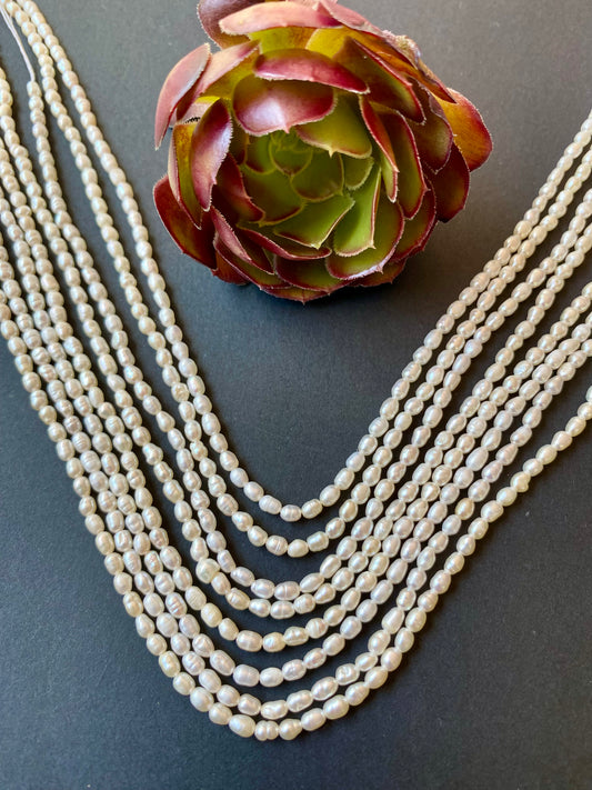 Beautiful strands of  2.5-2.75mm pearl beads resting on a sleek black background, showcasing their lustre.