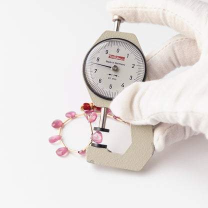 A dial gauge measures the Ruby Faceted Briolette 5.8-8.5mm gemstone.