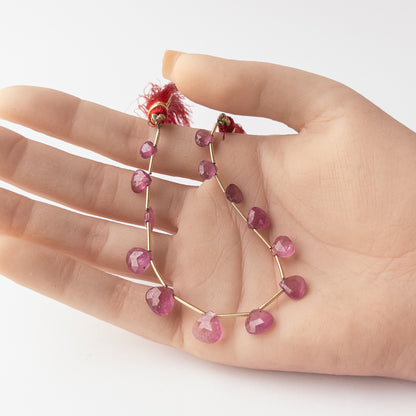 A person holds delicate pieces of Ruby beads, showcasing their faceted briolette design.