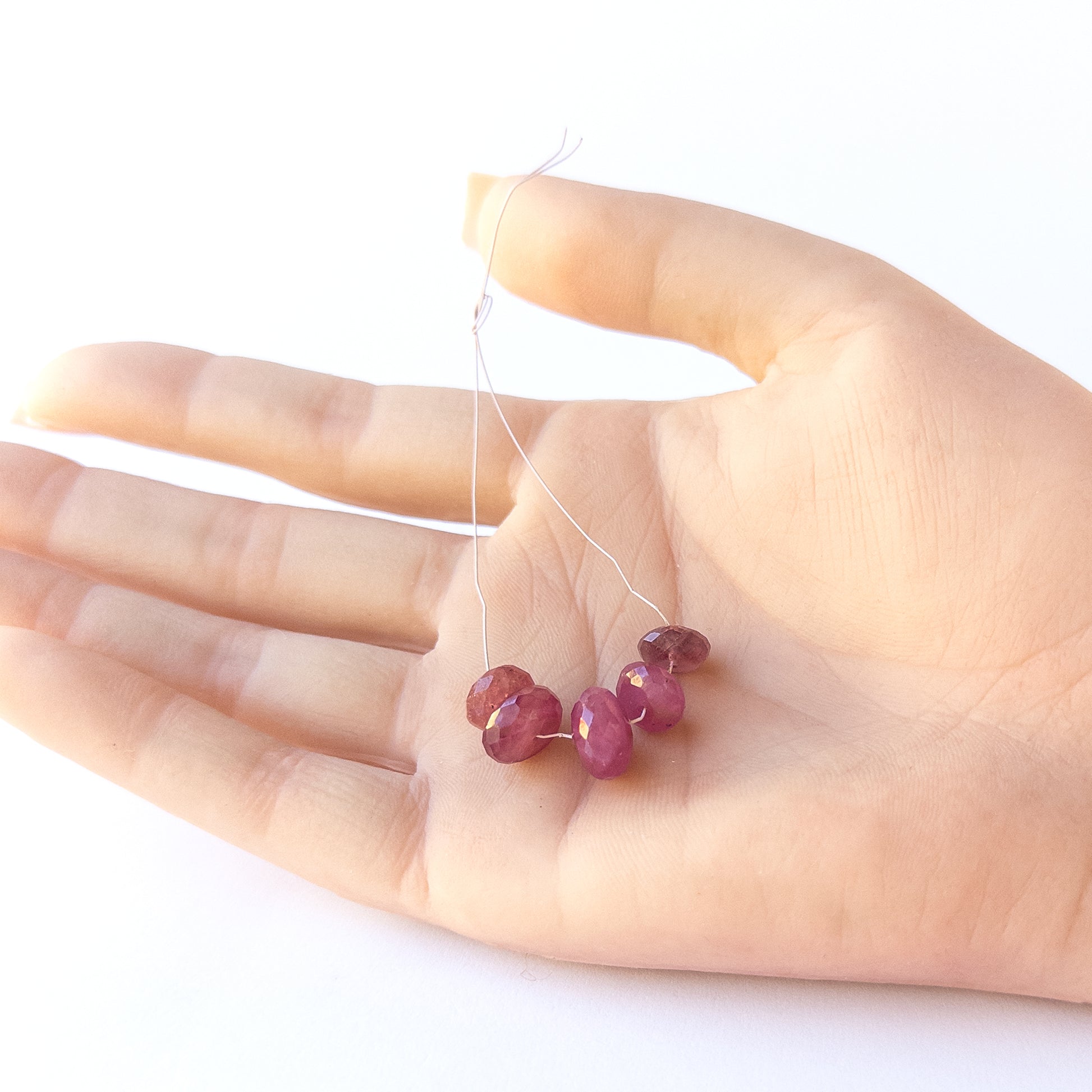 A person holds delicate pieces of Ruby beads, showcasing their faceted rondelle design.