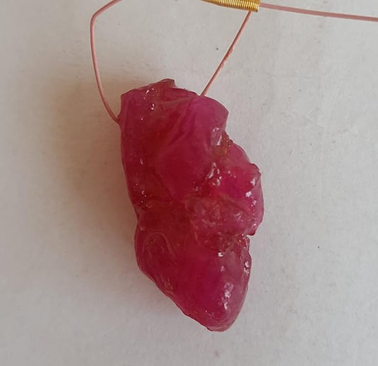 A vibrant ruby stone, attached to a luxurious gold tassel, showcasing its beauty and elegance.