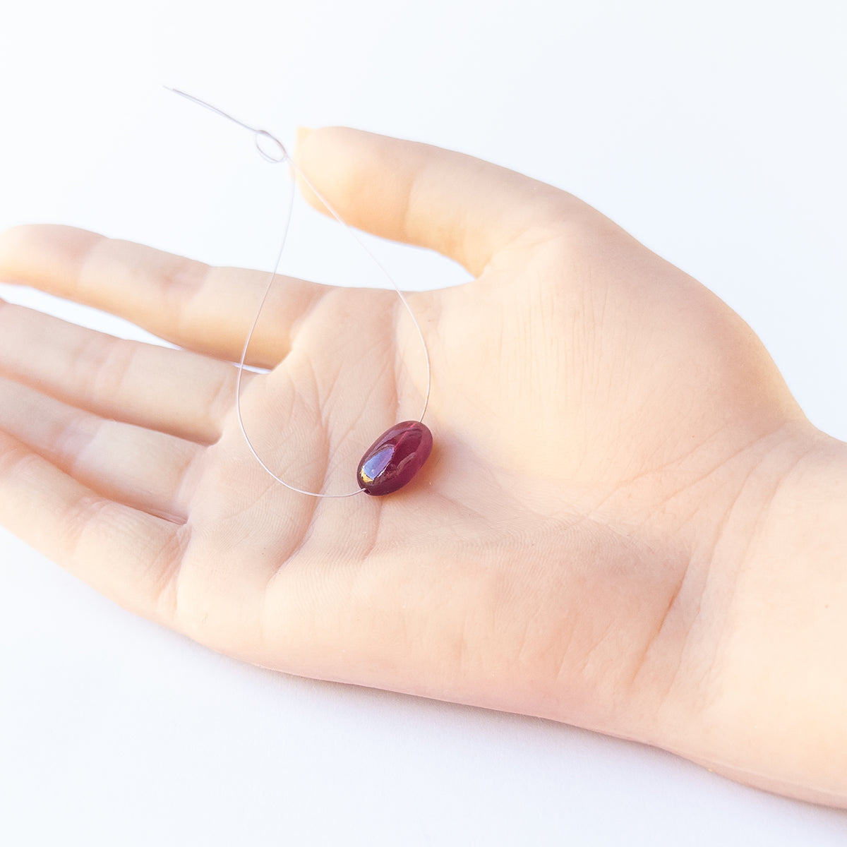 A person holds delicate pieces of Ruby beads, showcasing their smooth tumble design.