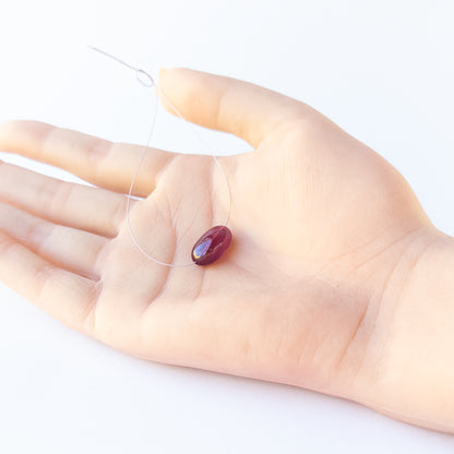 A person holds delicate pieces of Ruby beads, showcasing their smooth tumble design.