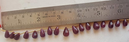 Close-up of a measuring rulers beside colourful precious beads, ruby tear drop shaped gemstone beads.