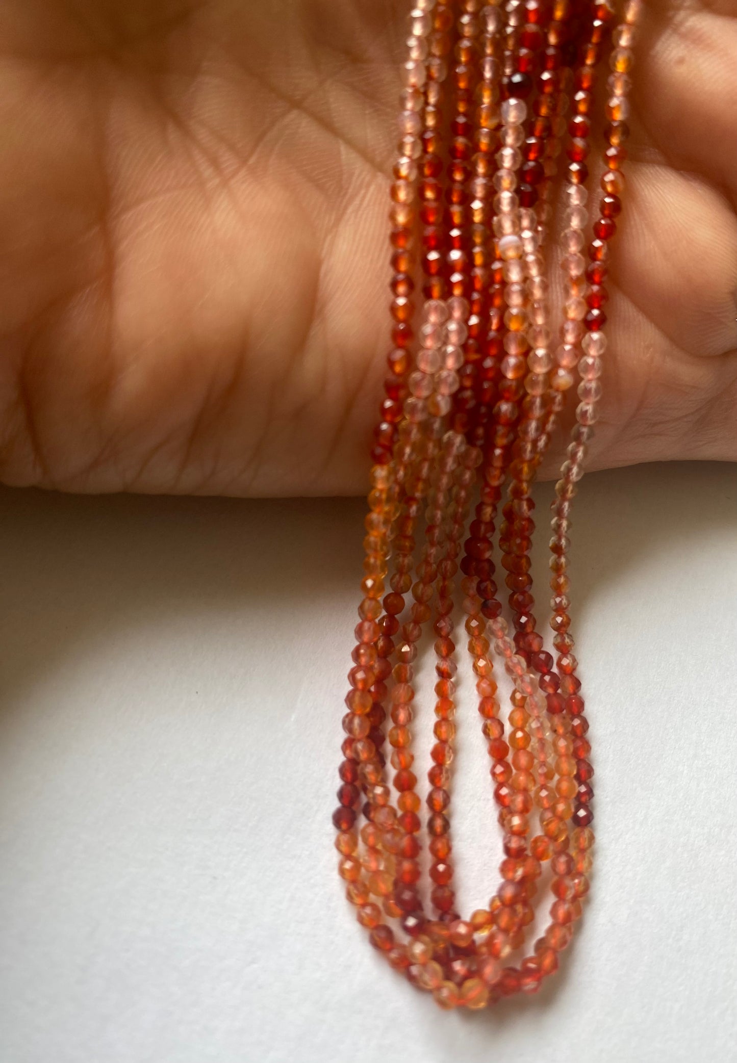 A hand displays beautiful strands of fiery Carnelian rondelle beads, crafted from faceted Carnelian rondelles.