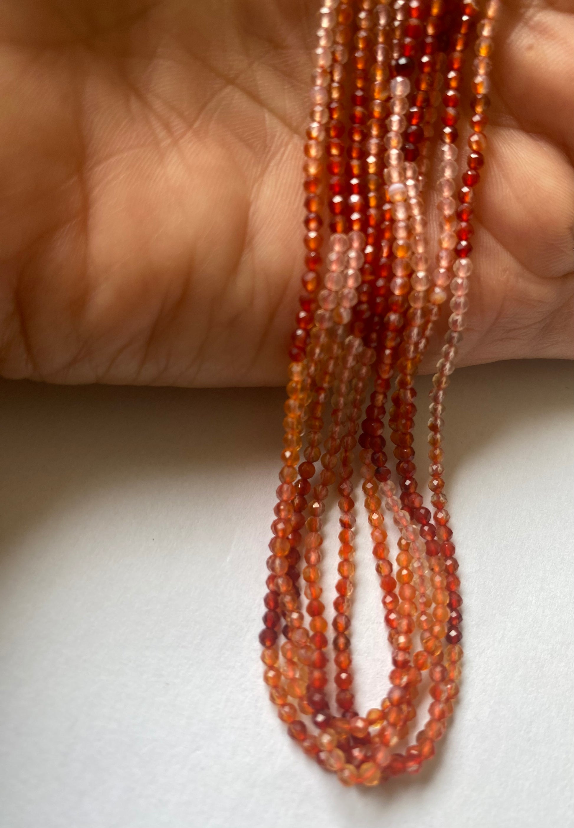 A hand displays beautiful strands of fiery Carnelian rondelle beads, crafted from faceted Carnelian rondelles.